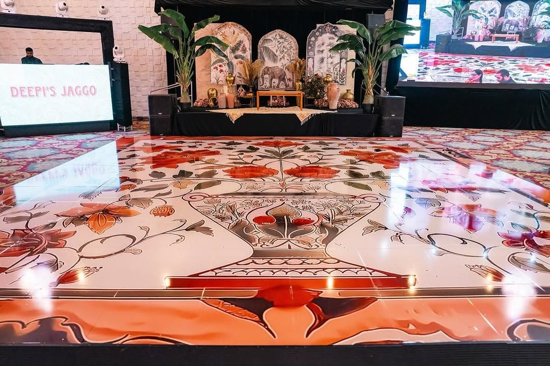 Coral and cream Mughal-pattern dance floor rental spanning the front of an event stage