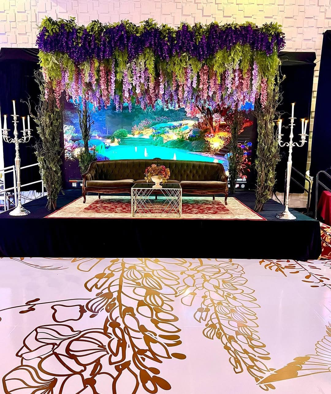 Blush dance floor rental with gold wisteria artwork beneath a hanging floral stage
