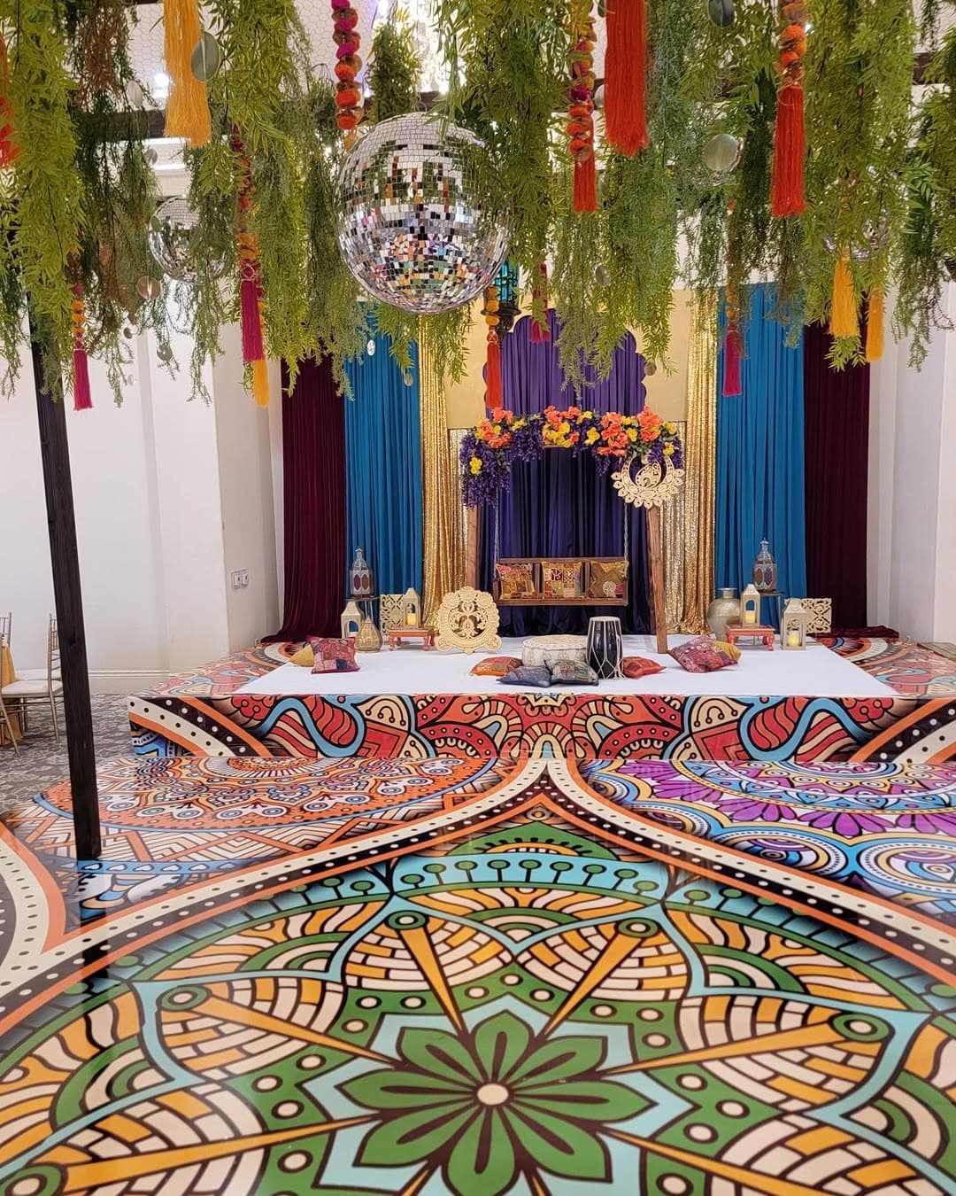 Multicoloured mandala dance floor rental under hanging greenery and tassels