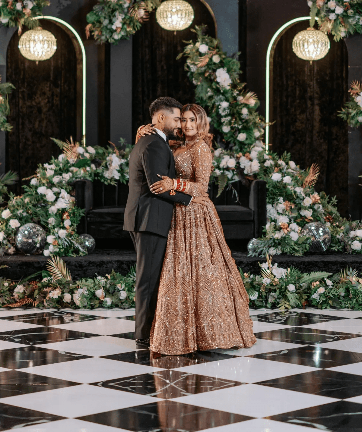 Couple dancing on elegant black and white checkered dance floor wrap with crystal chandeliers and lush floral backdrop