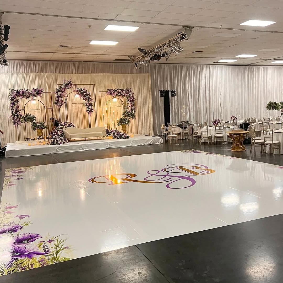 Glossy white dance floor rental with a gold and purple monogram at the centre of a ballroom reception