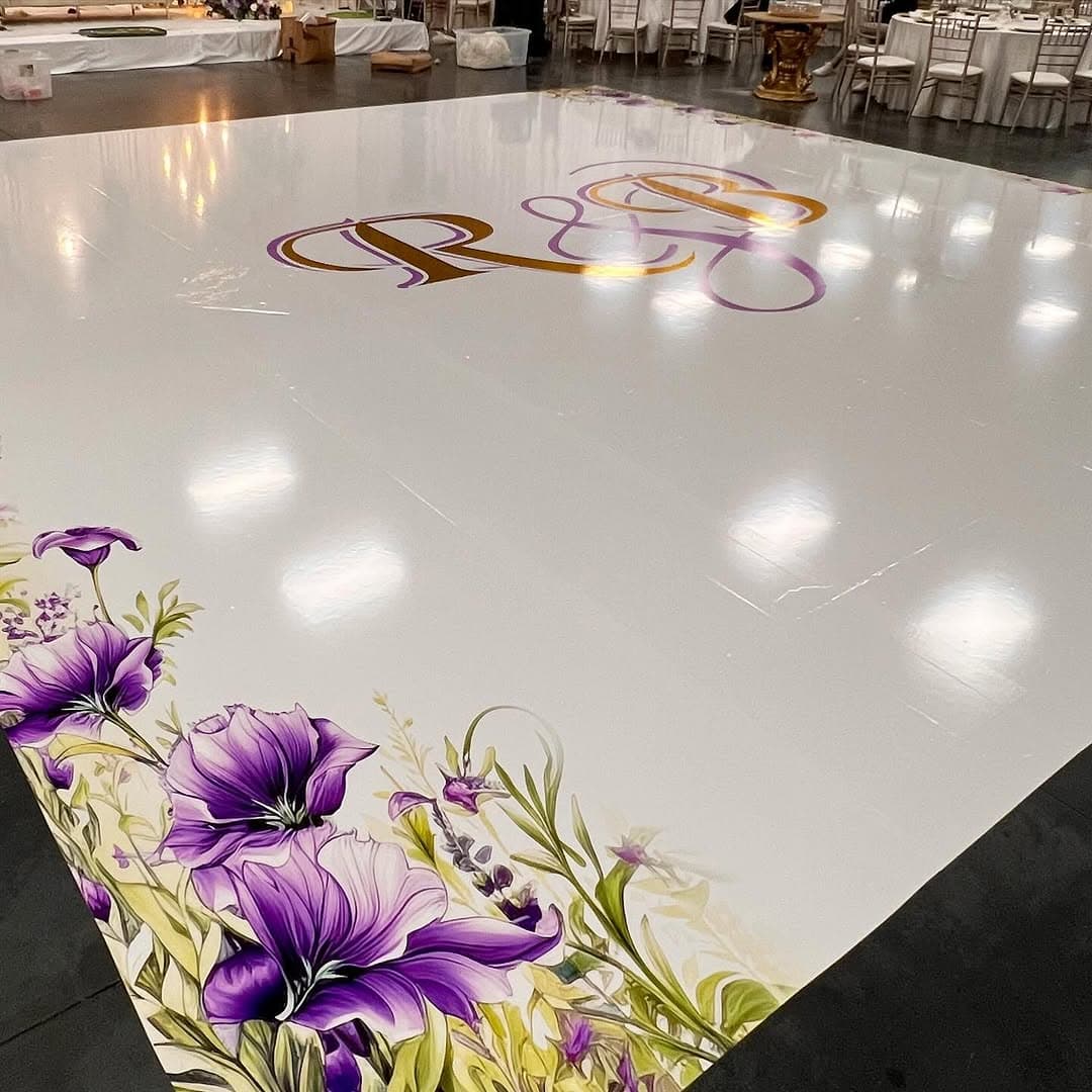 White dance floor rental with purple lilies painted along the border and a gold monogram