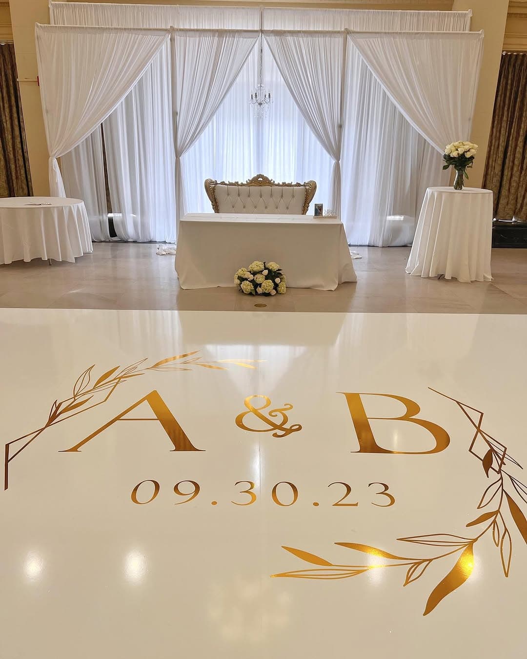 Cream dance floor rental with a gold monogram and wedding date inside an olive-branch wreath